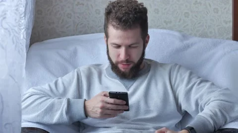 Young man talking on cellphone and drinking coffee on chair at home Stock Footage 68882095