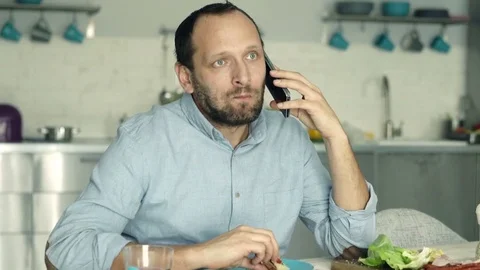 Young man talking on cellphone and eating breakfast in the kitchen Stock Footage 74153289