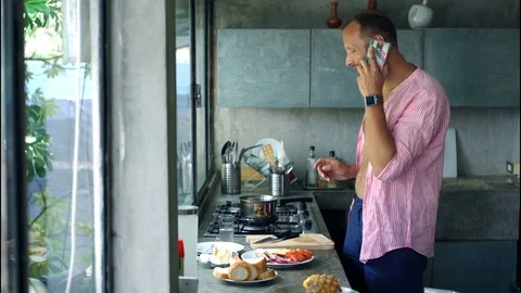 Young man talking on cellphone and preparing breakfast in the kitchen, 4K Stock Footage 74850052