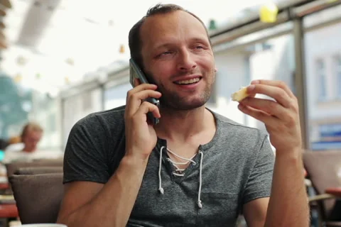 Young man talking on cellphone, eating sandwich in cafe NTSC Video stock 40344952