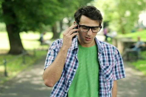 Young man talking on cellphone in the park, steadicam shot NTSC 스톡 동영상 11824073