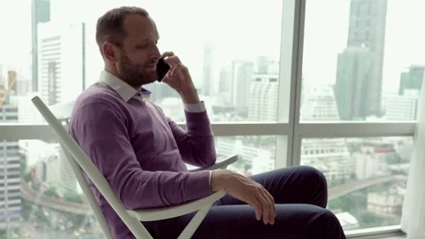 Young man talking on cellphone sitting on the chair at home Stock Footage 99839746