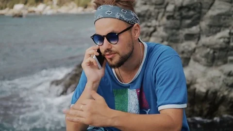 Young man talking on cellphone standing on beach near sea Stock Footage 79405910