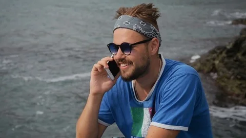 Young man talking on cellphone standing on beach near sea Stock Footage 79406285