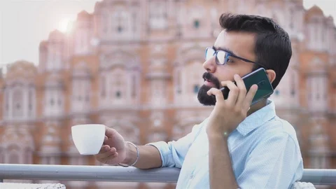 A young man talking with client on mobile while taking sip of a coffee Video stock 94130746