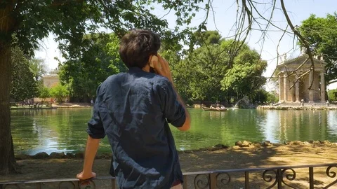 Young Man talking on her smartphone by a Pond in a park in Rome Video stock 77499949