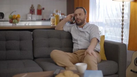The young man talking on his cell phone while sitting on his seat at home. Stock Footage 148120530
