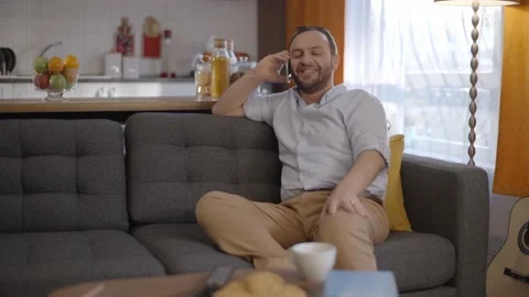 The young man talking on his mobile phone while sitting on his seat at home. Stock Footage 148120704