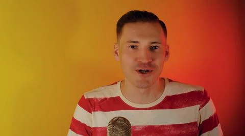 Young man talking into microphone on camera. Emotional blogger recording content Stock Photos