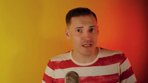 Young man talking into microphone on camera. Emotional blogger recording content Foto stock
