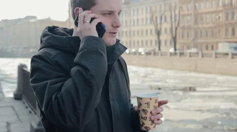 Young man talking on a mobile cell phone and enjoying a hot drink Stock Footage 61865366