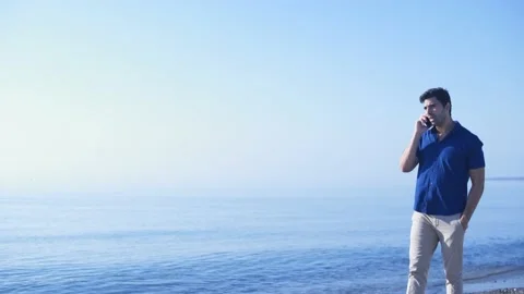 Young man talking on mobile phone while walking on beach Stock Footage 133261537