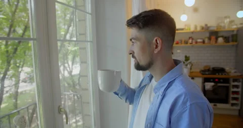 Young man talking on a mobile phone in the morning at a window with coffee Stock Footage 157651122
