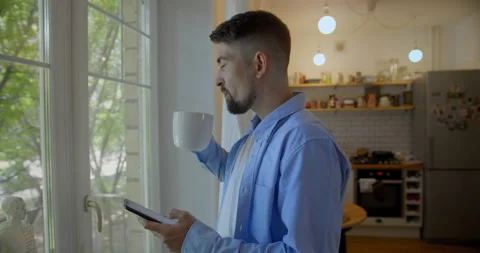 Young man talking on a mobile phone in the morning at a window with coffee Stock Footage 157651183
