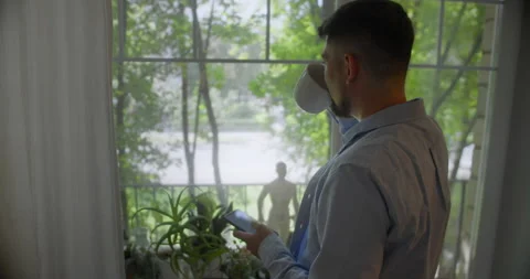 Young man talking on a mobile phone in the morning at a window with coffee Stock Footage 157651355