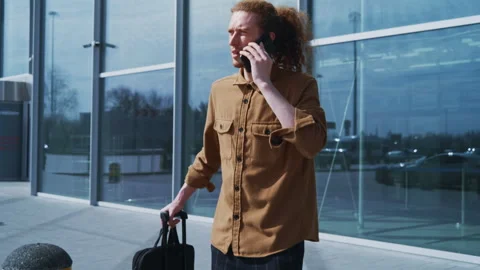 Young man talking on phone arriving at airport terminal with luggage Video stock 334567210