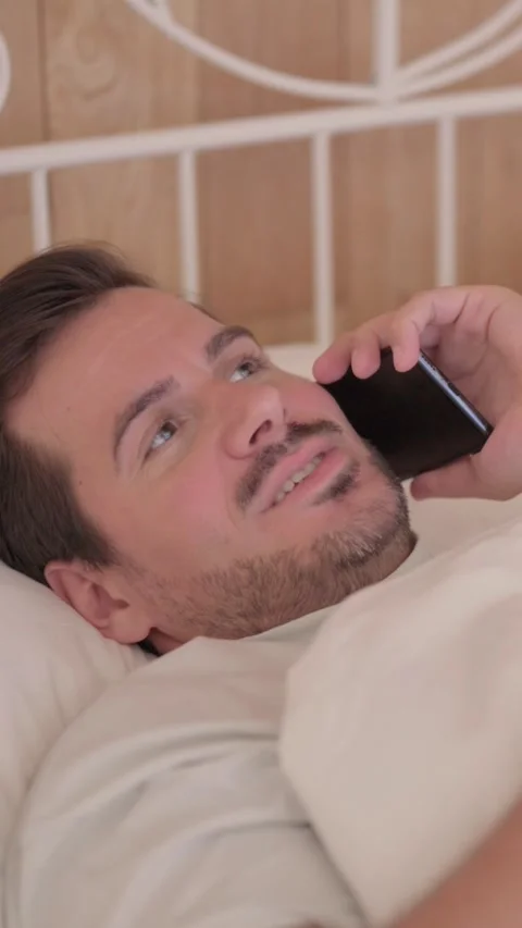 Young Man Talking on Phone in Bed, vertical video Stock-Footage 328564990