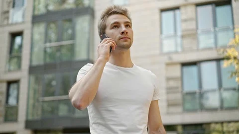 Young man talking on phone, checking his watch and goes away 動画素材 98305101