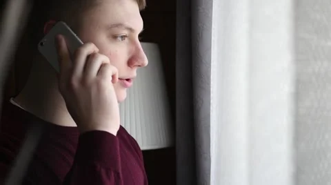 Young man talking on the phone. He is standing next to the window. Stock Footage 61281164