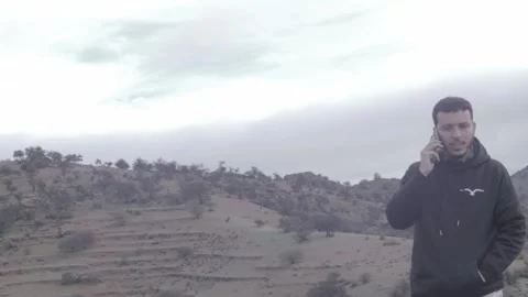 Young Man Talking on Phone on Misty Mountain Hilltop, Tiznit, Morocco Video stock 332770034