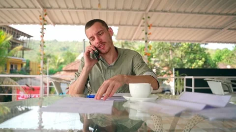 A young man talking on the phone, pointing his finger at a notebook. Video stock 231336533