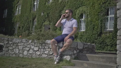 Young man talking by phone, sitting on the wall. 库存影片 65522657