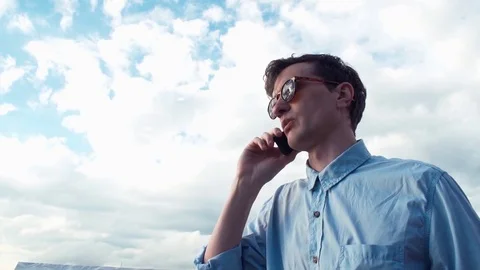 Young man talking on phone standing outdoors. Bright sky at background. Stock Footage 77167287