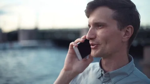 Young man talking on phone standing outdoors. Bridge at background. Stock Footage 79930060