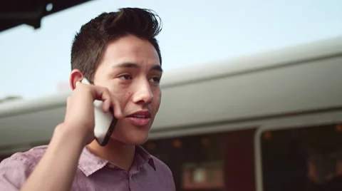 A young man talking on a phone while walking past a train, in slow motion Video stock 57508944