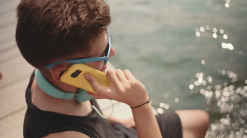 Young man talking on phone while sitting by a lake. Stock Footage 94171726
