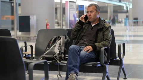 Young man talking with phone while waiting for plane in airport terminal Stock Footage 98322305