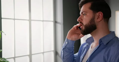 Young man talking on phone while standing near window, getting nervous during Stock-Footage 151349642