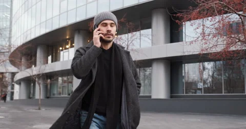 Young man talking by phone while walking in the street near business center Video stock 178574544