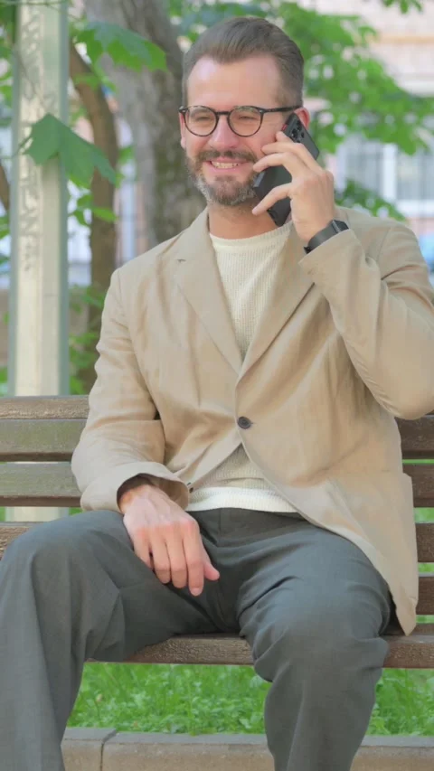 Young Man Talking on phone while Sitting Outdoor, Vertical Video Stock Footage 319018601