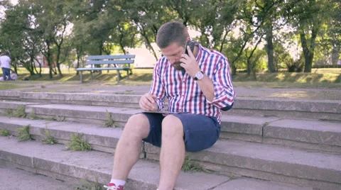 Young man talking by smartphone and browsing tablet. Slider and pan shot, right. 動画素材 67243109