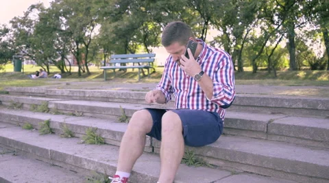 Young man talking by smartphone and browsing tablet. 库存影片 67243283