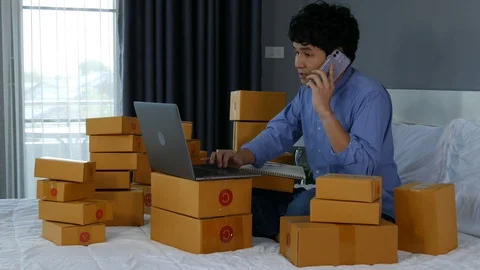 Young man talking on smartphone and using laptop computer to selling product  Stock Footage 130099545