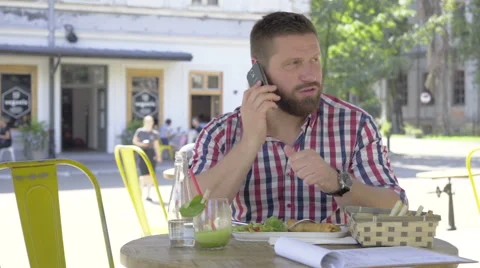 Young man talking by smartphone, during lunch, slider shot left. 库存影片 67604159