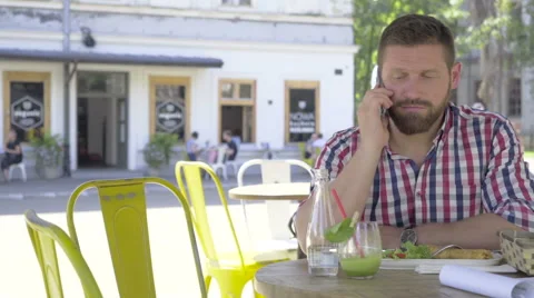 Young man talking by smartphone, during lunch, slider shot right. 库存影片 67604162