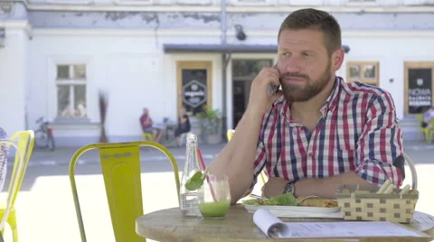 Young man talking by smartphone, during lunch, slider and pan shot. 库存影片 67604176