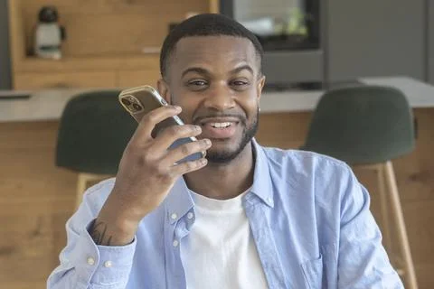 Young man talking on smartphone in modern kitchen, smiling as he chats with.. Stock Photos