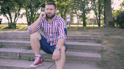 Young man talking by smartphone, sitting on stairs. Vídeo Stock 67241105