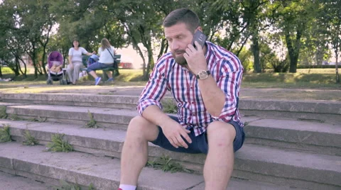 Young man talking by smartphone, sitting on stairs. Slider shot. 库存影片 67241305