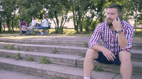 Young man talking by smartphone, sitting on stairs. Slider shot. Video stock 67241330