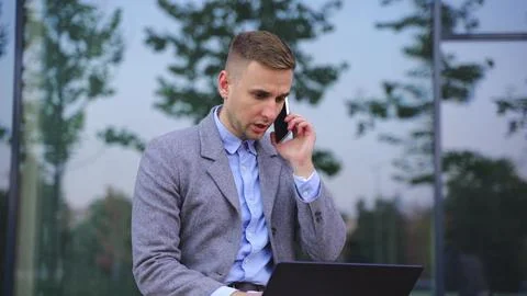 Young man talking on the smartphone, using laptop outdoors. Slow motion Foto stock