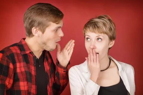Young man talking something to surprised woman on red 写真素材