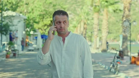 A young man talks on his smartphone on a tree-lined road. Stock Footage 166004579