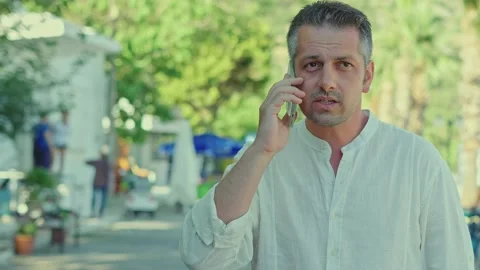 A young man talks on his smartphone on a tree-lined road. Stock Footage 166004600