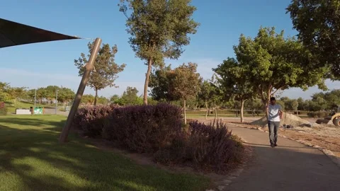 Young man talks on mobile phone while walking through a public park Stock Footage 133074774