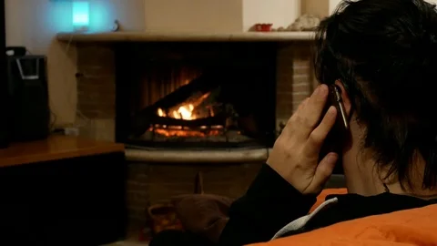 A young man talks on the phone sitting on the sofa in front of the fireplace Stock Footage 102231272